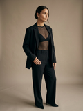 Model wearing the Vervain black mesh bodysuit with a tailored black suit.
